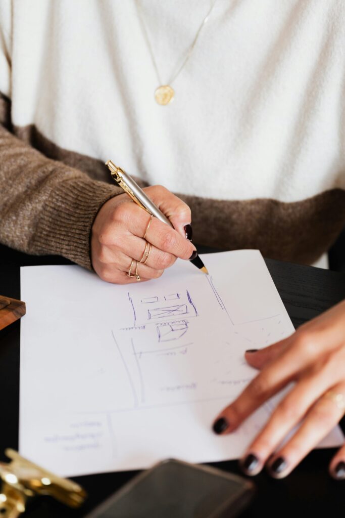 Image of a woman's hand holding a pen and sketching ideas on a notepad